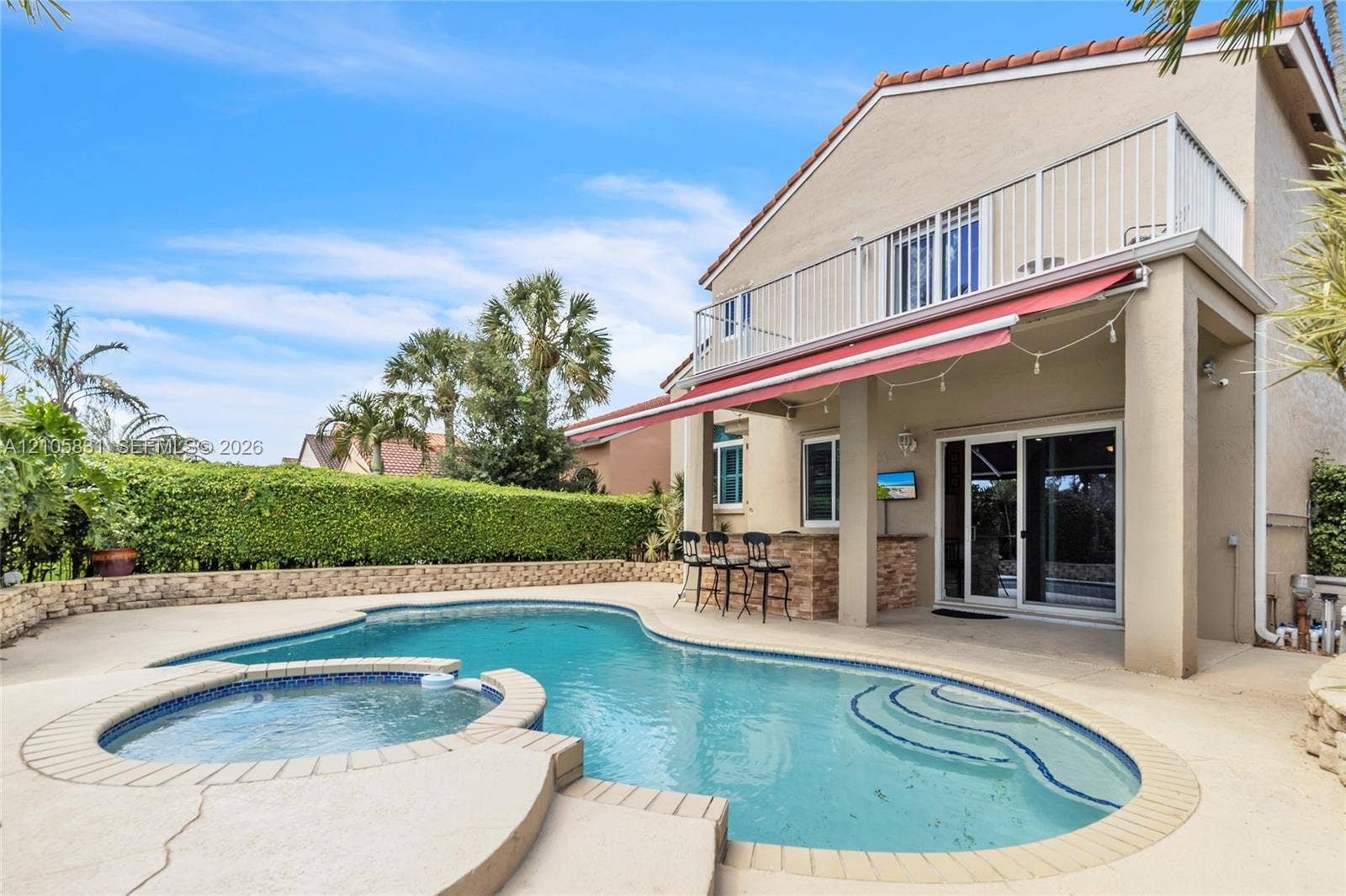 15612 SW 16th Court, Pembroke Pines, FL 33027 Backyard area featuring an in-ground swimming pool, attached spa, stone-veneer outdoor bar, retractable awning, and second-story balcony with metal railing
