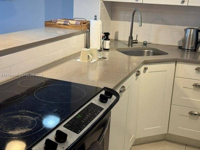 1400 S Ocean Drive, #1503, Hollywood, Hollywood, FL 33019 Kitchen featuring white shaker-style cabinetry, neutral-toned solid surface countertops, subway tile backsplash, stainless steel drop-in sink with a high-arch pull-down faucet, and a glass-top electric range