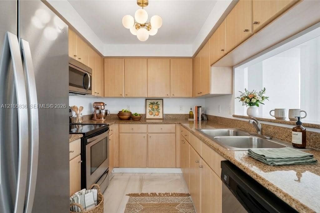 2475 Brickell Avenue, #704, Miami, FL 33129 Kitchen featuring light wood cabinetry, stone countertops, stainless steel appliances, a double-basin undermount sink, and a multi-globe light fixture