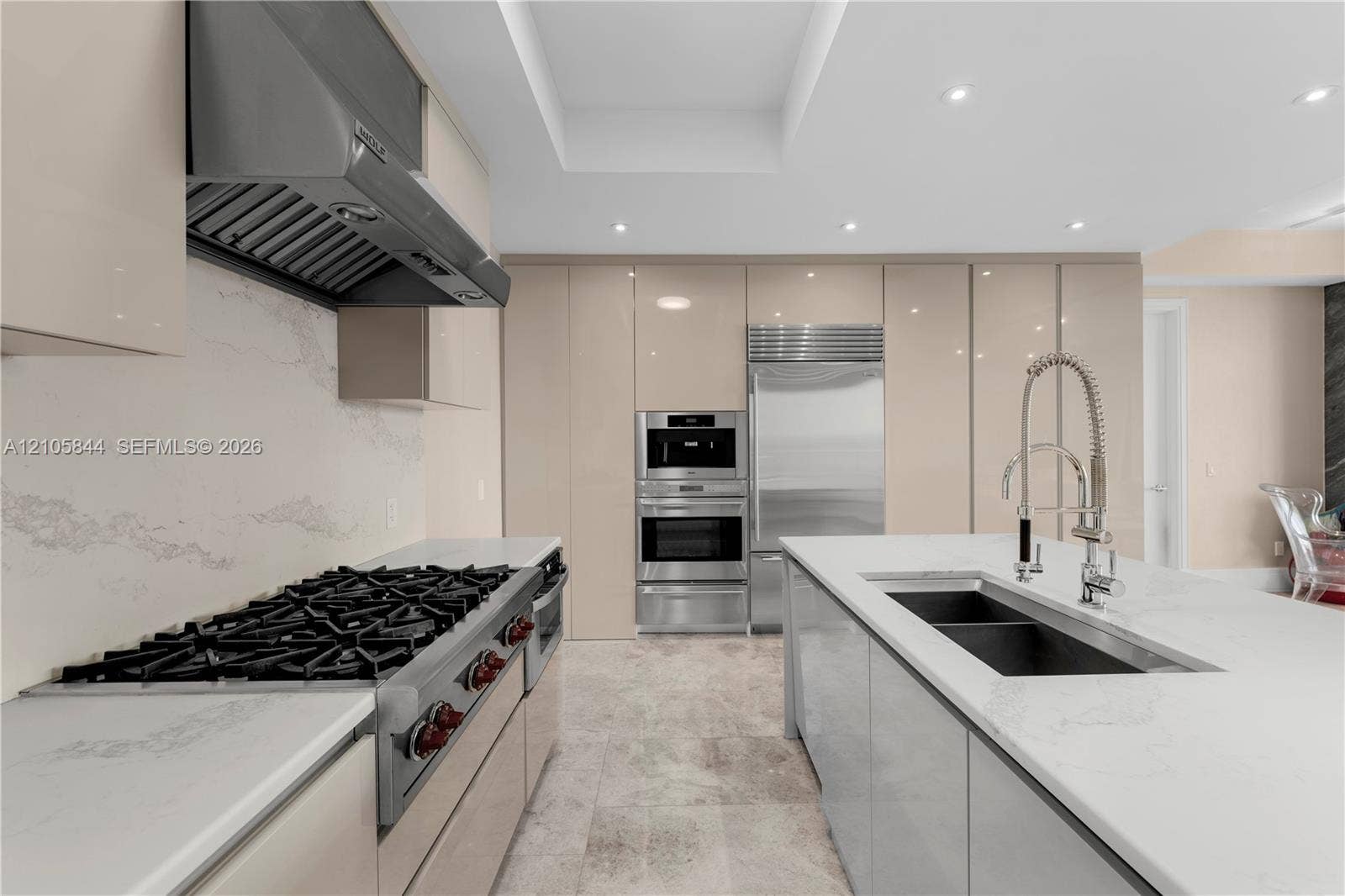 Bal Harbour, Bal Harbour, FL 33154 Kitchen featuring flat-panel cabinetry, a stainless steel gas range with a professional-grade hood, stone countertops with matching backsplash, built-in stainless steel appliances, and a central island with a double-basin undermount sink