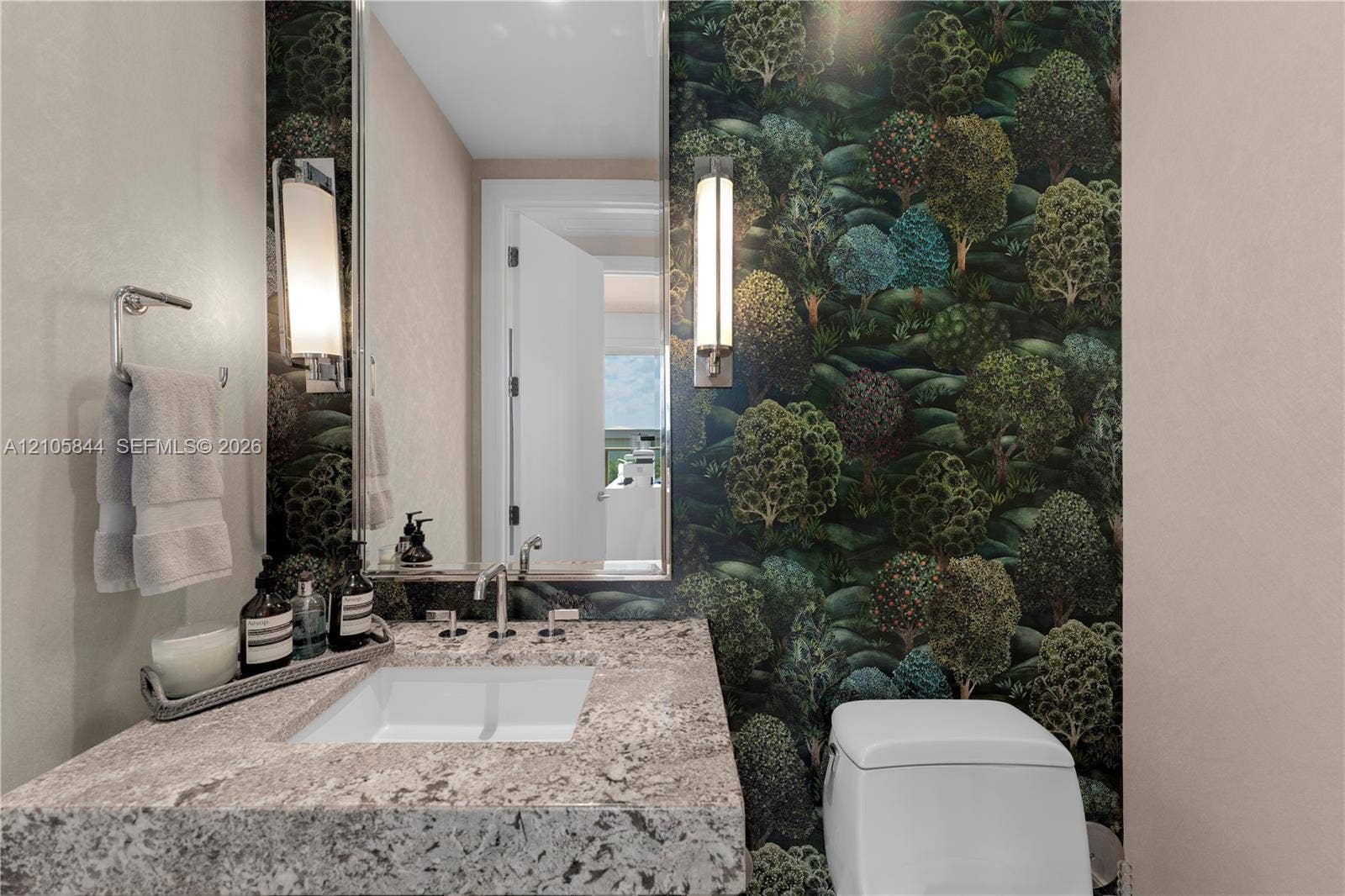 Bal Harbour, Bal Harbour, FL 33154 Stone-surfaced vanity with an integrated rectangular sink, wall-mounted metal faucet, floor-to-ceiling forest-motif wallpaper, and dual vertical wall sconces