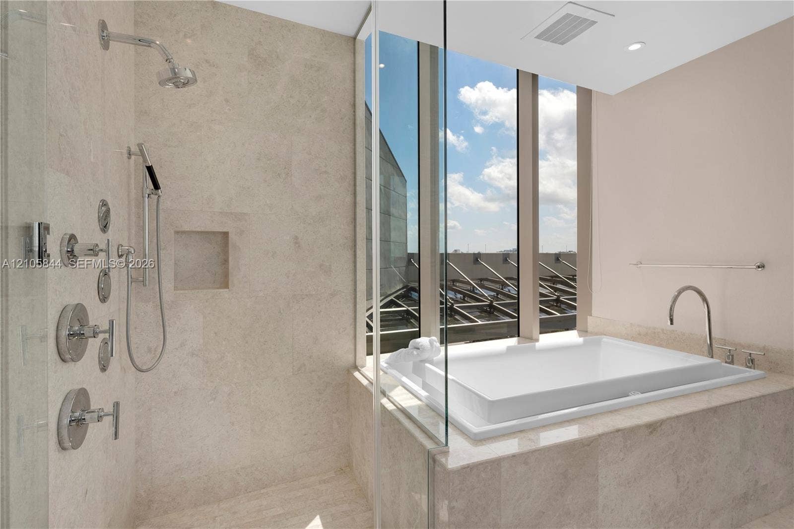 Bal Harbour, Bal Harbour, FL 33154 Walk-in shower featuring natural stone tiling, recessed wall niche, and multi-head chrome fixtures, accompanied by a drop-in soaking tub with floor-to-ceiling windows