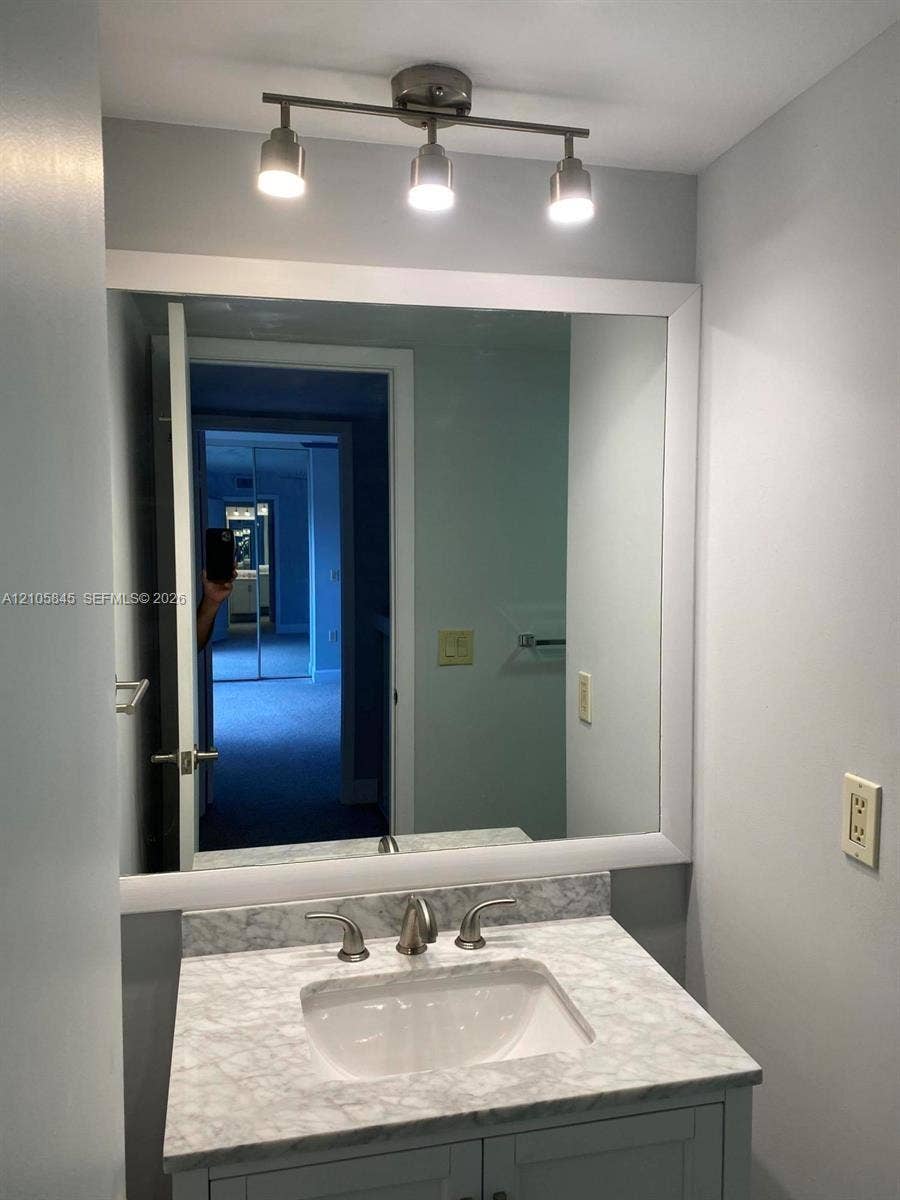 2001 20th Way, #2001, West Palm Beach, West Palm Beach, FL 33407 Vanity featuring a stone-look countertop, integrated rectangular sink, widespread metallic faucet, framed wall mirror, and three-light track fixture