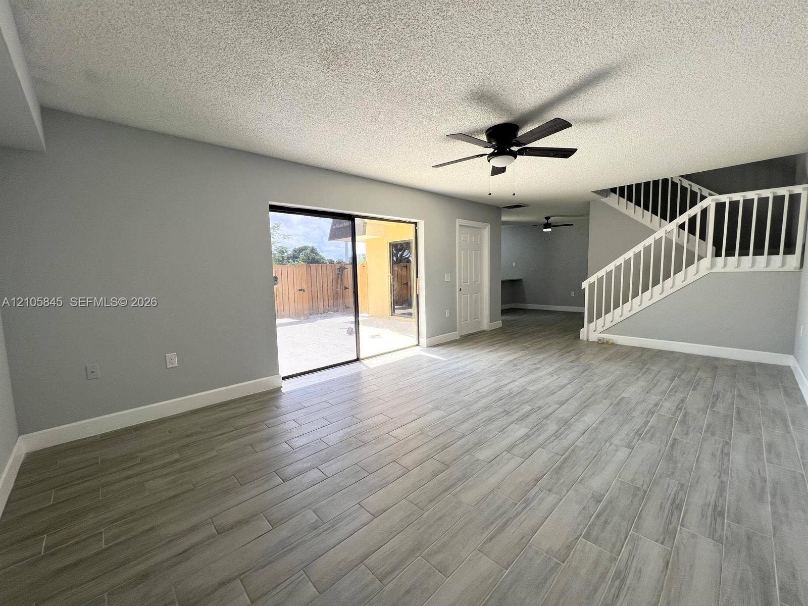 2001 20th Way, #2001, West Palm Beach, West Palm Beach, FL 33407 Open-concept interior featuring wood-finish tile flooring, a sliding glass door, white stair railing, and a ceiling fan