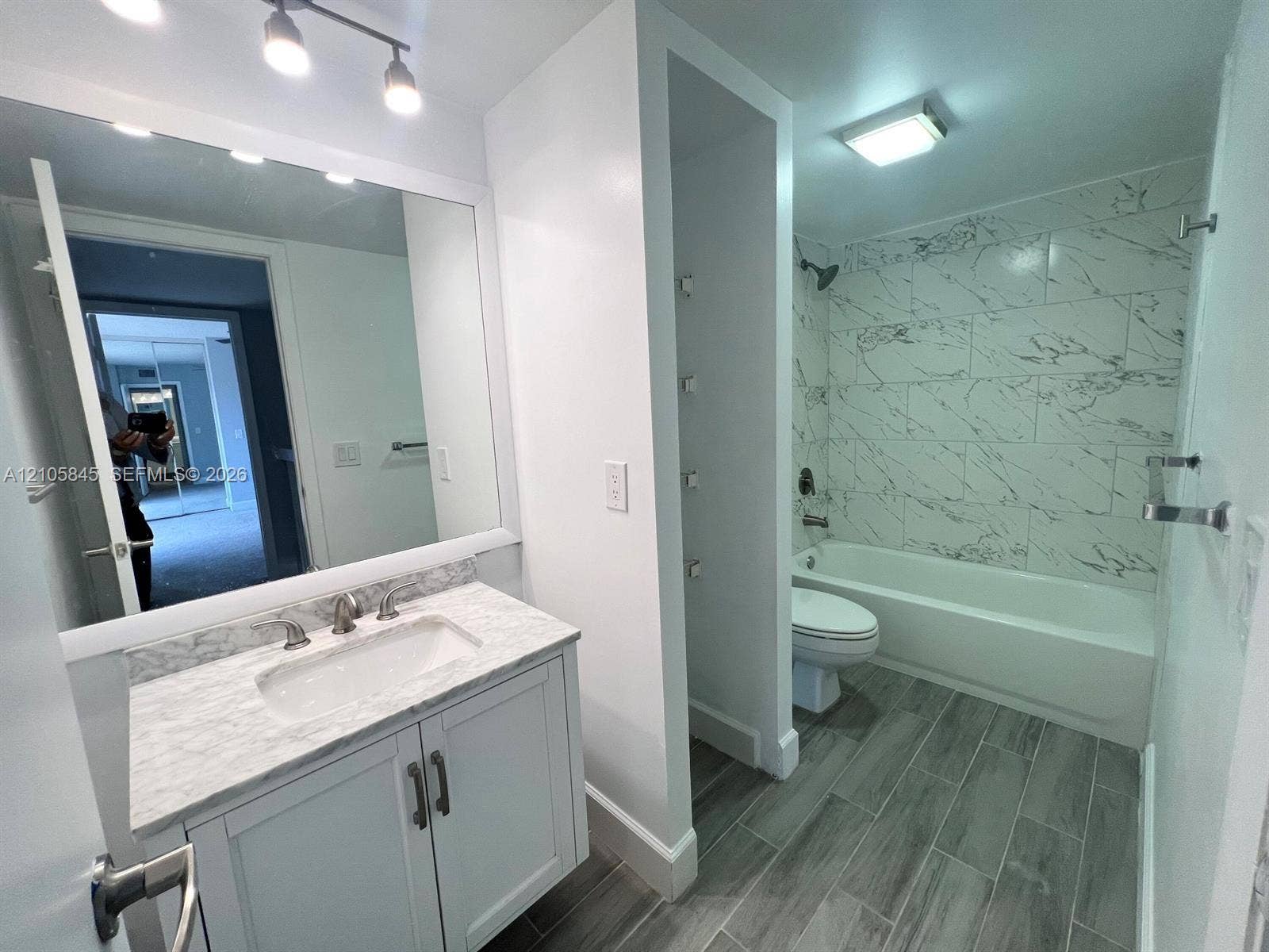 2001 20th Way, #2001, West Palm Beach, West Palm Beach, FL 33407 Bathroom featuring a vanity with stone-finish countertop, undermount sink, full-width mirror, tile-surround bathtub, and wood-finish flooring