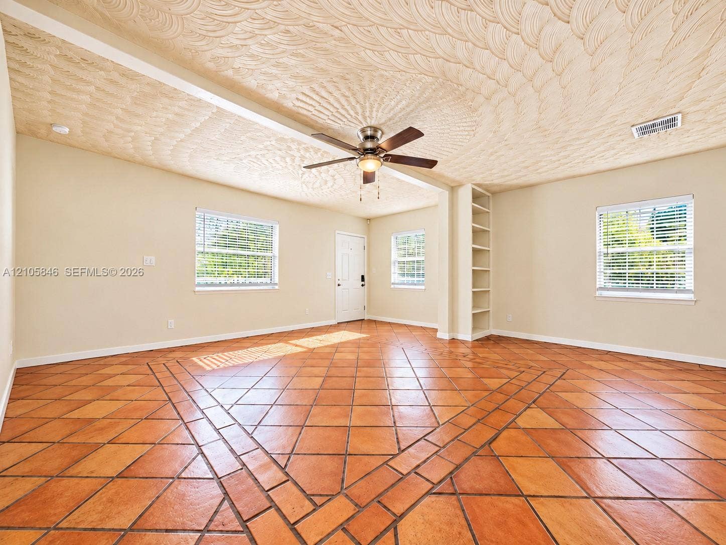 Interior space featuring decorative textured ceiling, expansive ceramic tile flooring in a geometric pattern, built-in recessed shelving, and a ceiling fan with integrated lighting