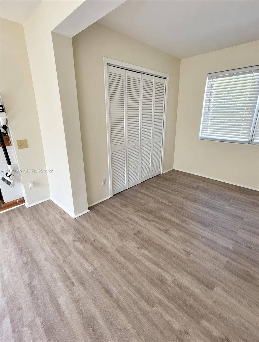 Neutral-toned walls, wood-finish flooring, and white louvered bifold closet doors, complemented by a window with horizontal blinds
