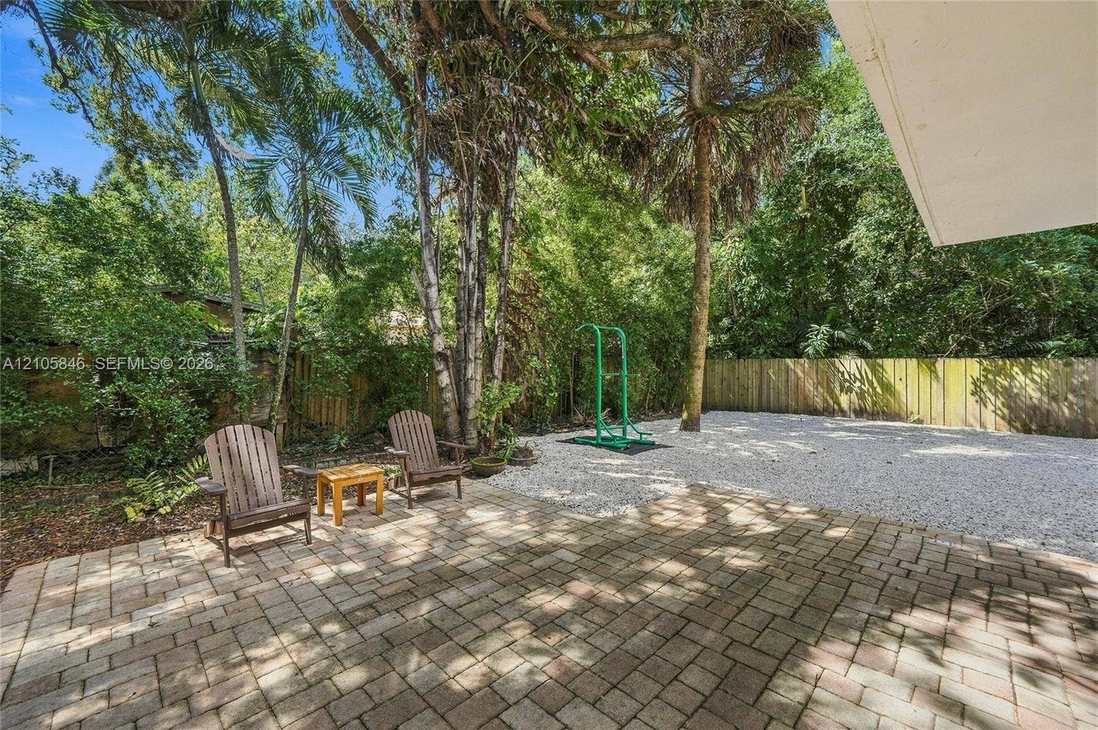 Backyard featuring a brick paver patio, crushed stone ground cover, perimeter wood fencing, and mature trees