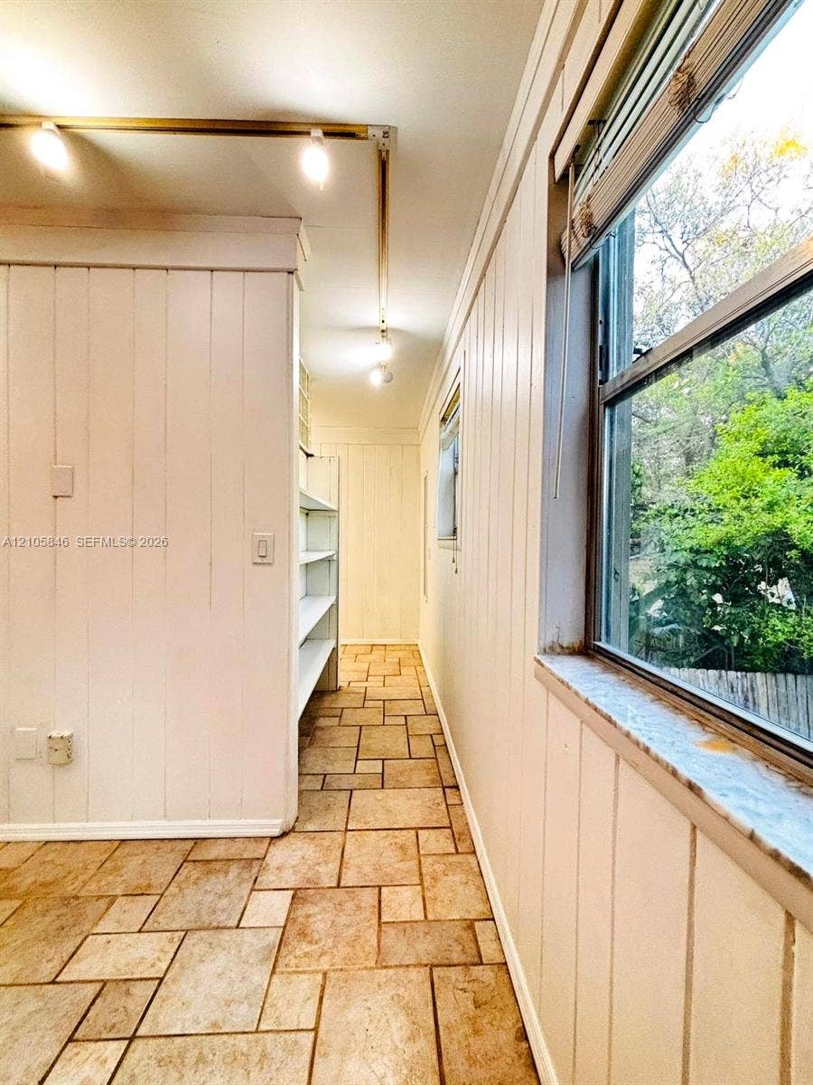 Vertical wood-paneled walls, tile flooring in a running bond pattern, built-in shelving, track lighting, and window with stone sill