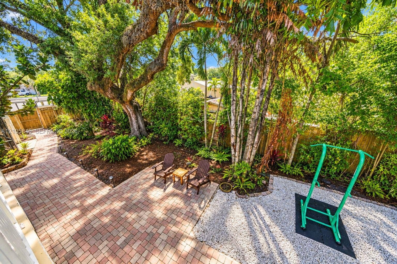Landscaped backyard featuring paver patio, gravel ground cover, mature trees, and wooden perimeter fencing