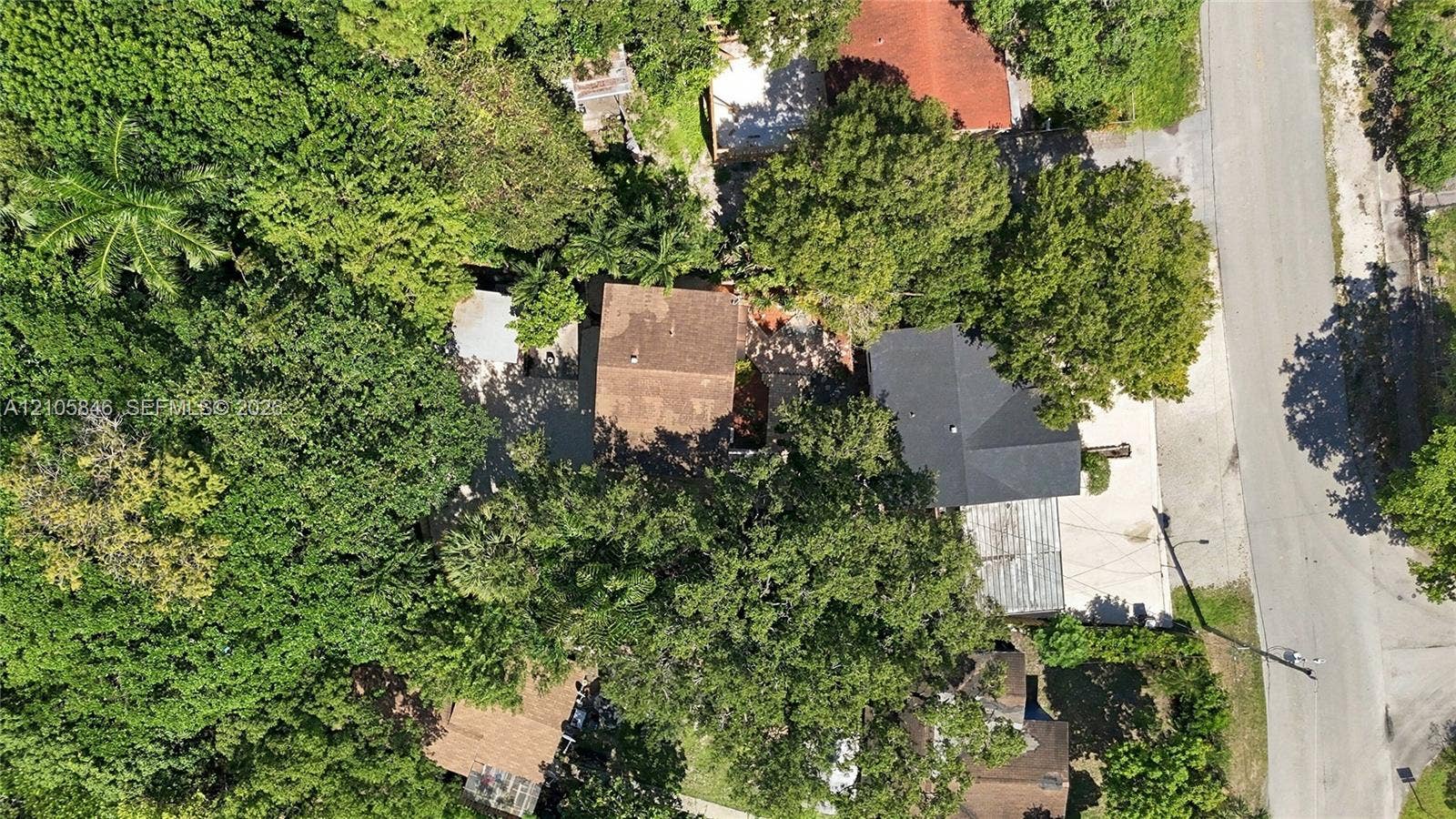 Aerial perspective featuring a residential lot with mature canopy trees, asphalt shingled roofing, and paved driveway access