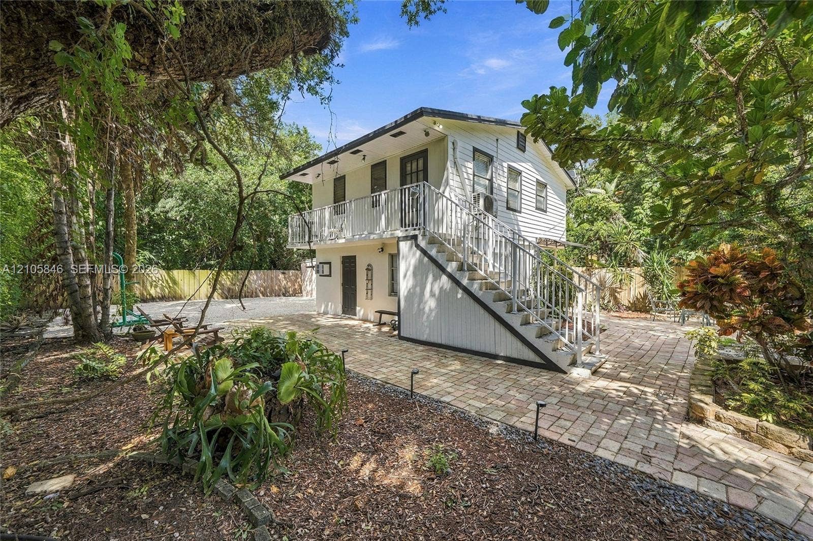 Two-story detached structure featuring horizontal siding, exterior staircase with metal railing, upper-level balcony, and a paved brick patio