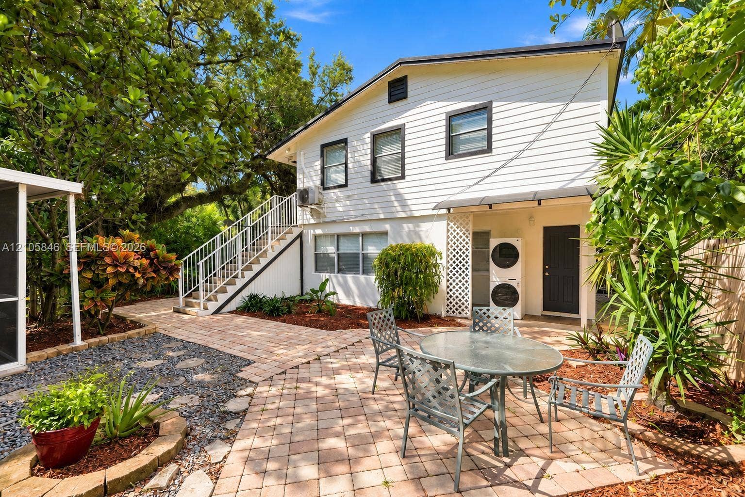 Exterior two-story structure featuring horizontal siding, a paved brick patio, an exterior metal staircase with railings, and mulched landscaping beds