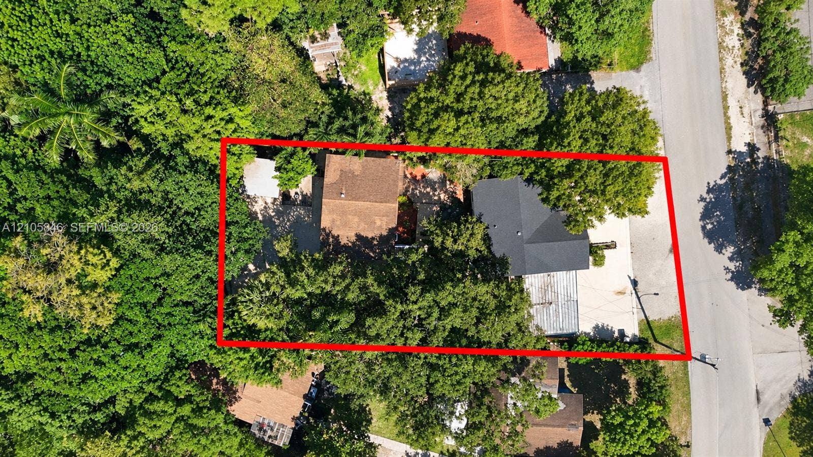 Aerial view of a parcel featuring mature trees, substantial canopy coverage, and paved driveway space