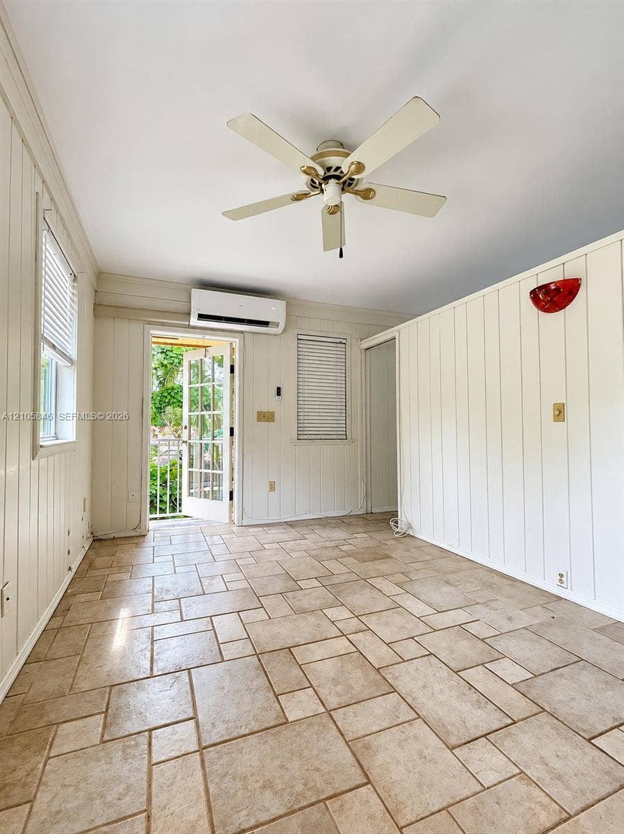 Vertical tongue-and-groove wall paneling, modular tile flooring, wall-mounted ductless HVAC unit, ceiling fan with light fixture, and multi-pane glass door