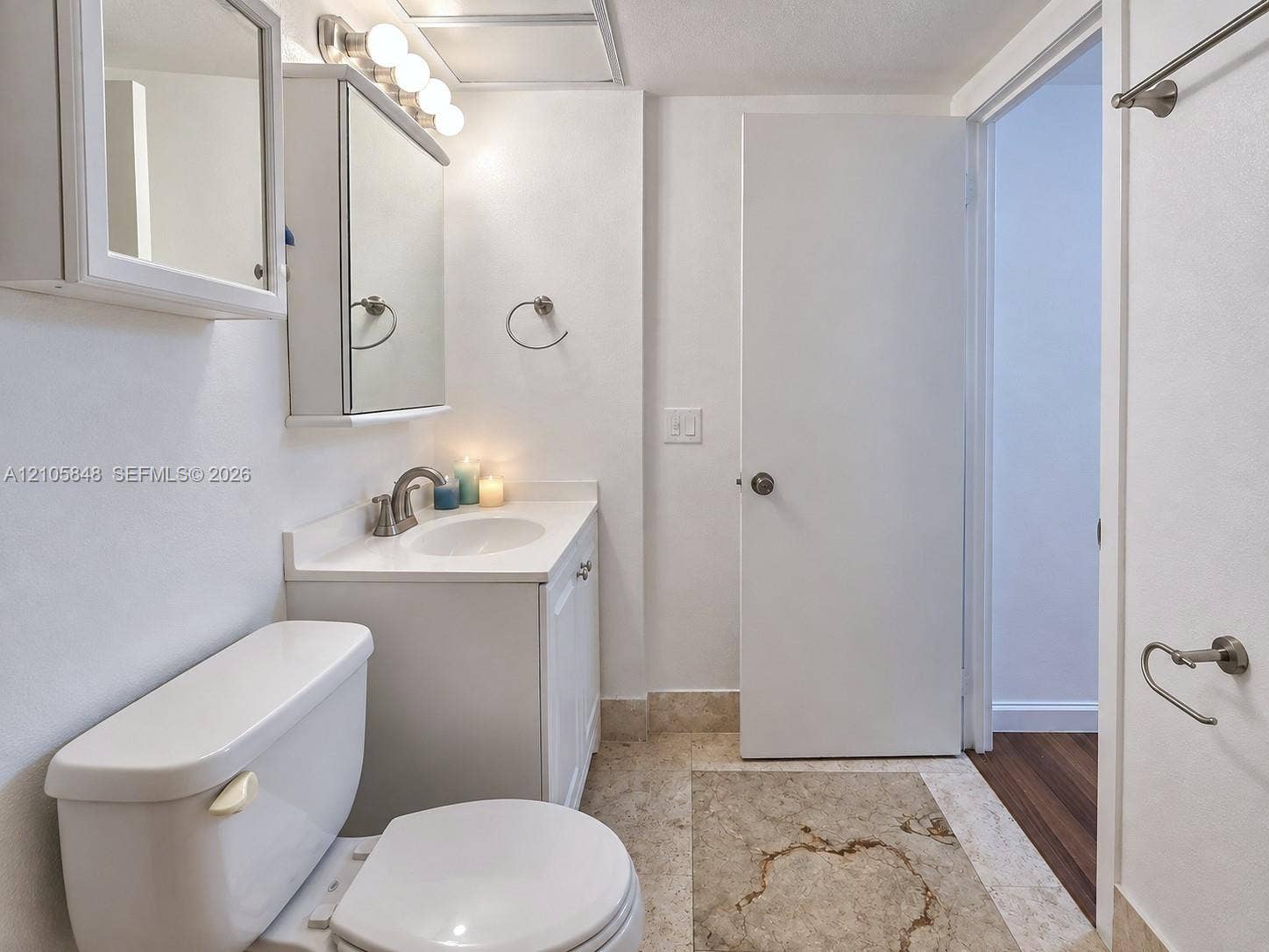 Bathroom featuring a vanity with a white countertop and integrated sink, mirrored medicine cabinet, brushed nickel-finish hardware, and stone-tile flooring