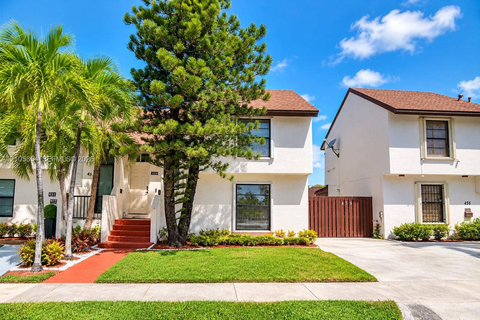 454 NW 97th Place, Miami, FL 33172 Multi-level exterior featuring light-toned stucco siding, a shingled roof, defined entryway with concrete steps, and integrated privacy fencing