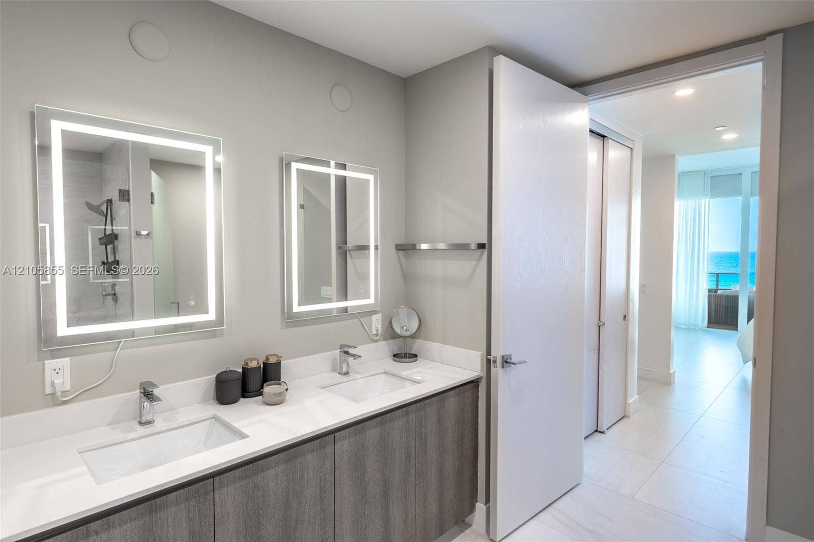 17550 Collins Avenue, #703, Sunny Isles Beach, Sunny Isles Beach, FL 33160 Bathroom featuring a double vanity with integrated rectangular sinks, white stone-finish countertop, dual backlit mirrors, and gray wood-finish cabinetry
