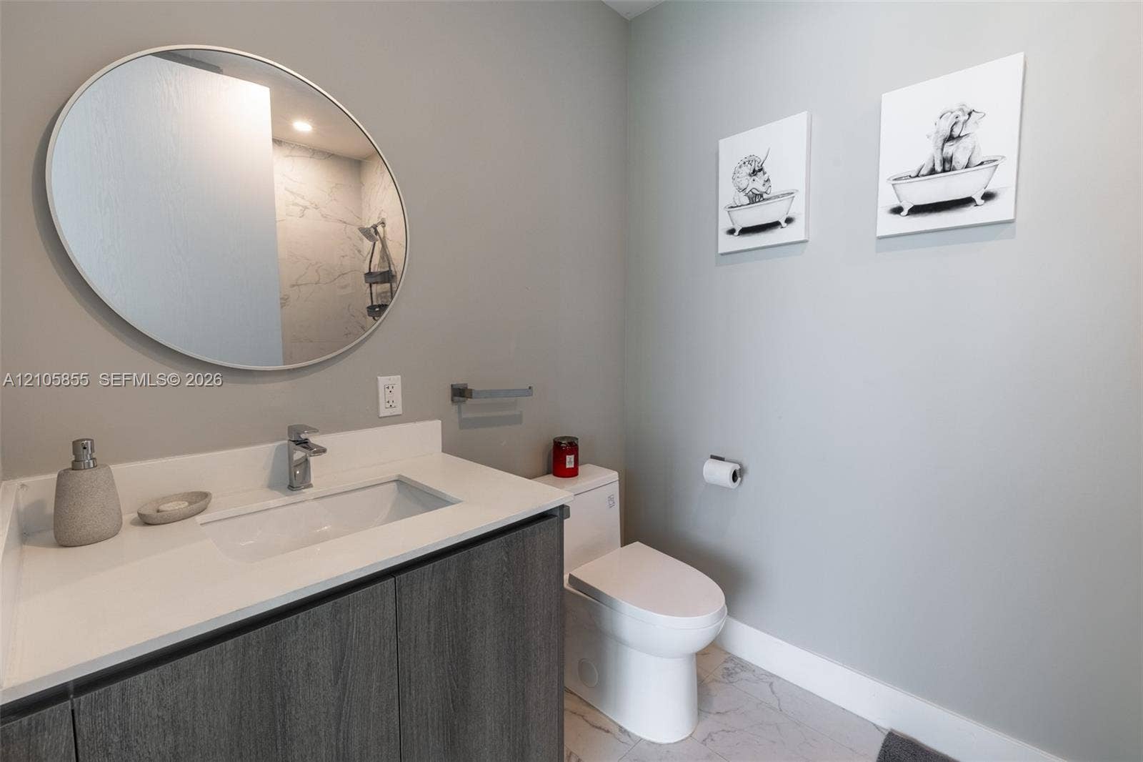 17550 Collins Avenue, #703, Sunny Isles Beach, Sunny Isles Beach, FL 33160 Bathroom featuring a dark wood-finish vanity with a white countertop and rectangular integrated sink, circular wall-mounted mirror, polished chrome faucet, and stone-finish flooring