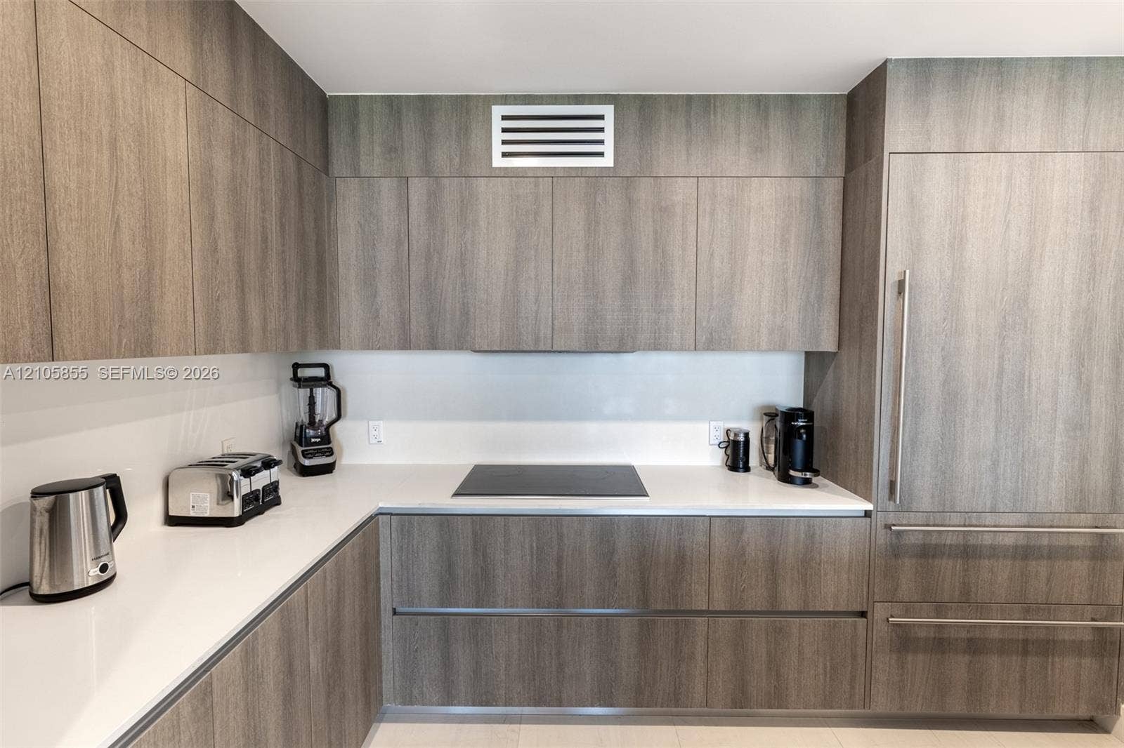 17550 Collins Avenue, #703, Sunny Isles Beach, Sunny Isles Beach, FL 33160 Contemporary kitchen featuring flat-panel wood-finish cabinetry, white solid-surface countertops, a seamless back-painted glass backsplash, a built-in induction cooktop, and a panel-ready refrigerator