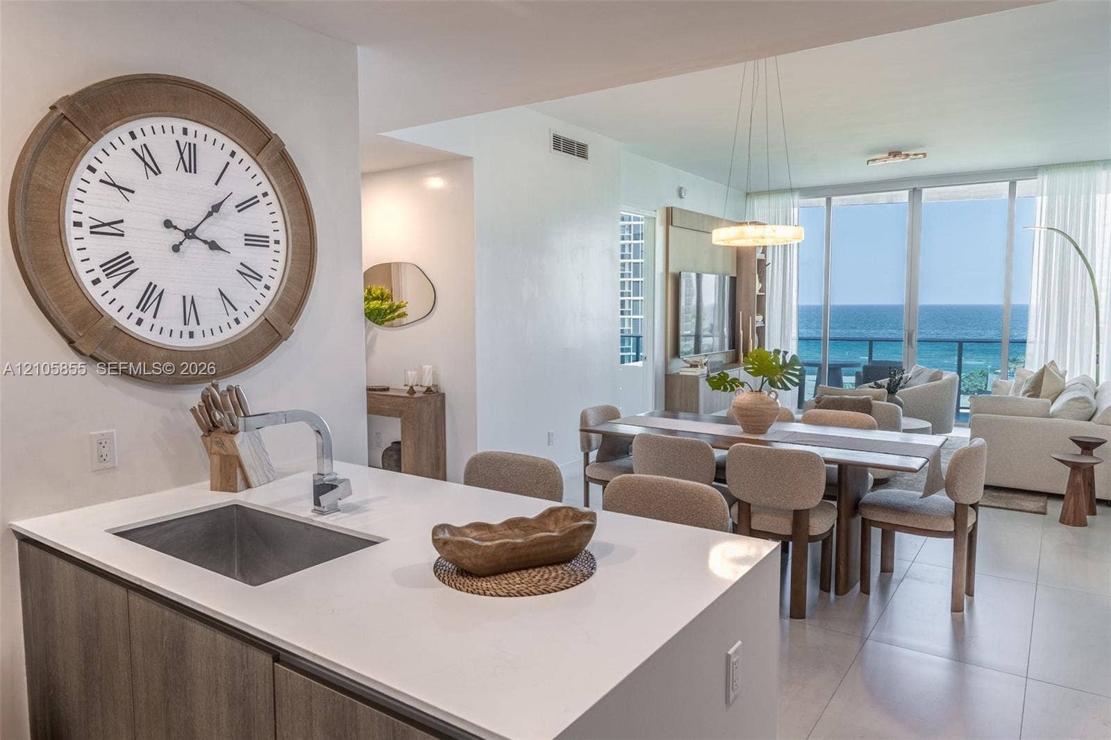 17550 Collins Avenue, #703, Sunny Isles Beach, Sunny Isles Beach, FL 33160 Kitchen island featuring a white countertop, under-mount sink, and modern faucet, complemented by wood-finish cabinetry and large-format tile flooring, complete with floor-to-ceiling glass sliding doors