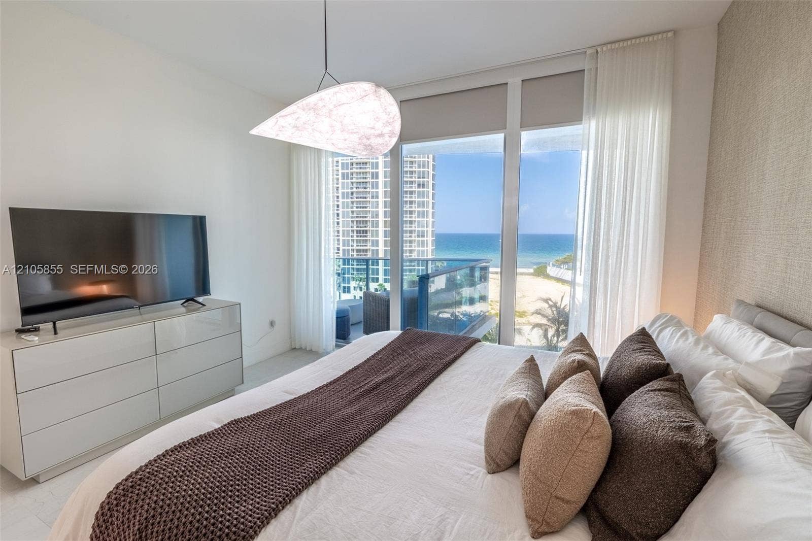 17550 Collins Avenue, #703, Sunny Isles Beach, Sunny Isles Beach, FL 33160 Floor-to-ceiling windows, sculptural pendant light, textured accent wall, and balcony featuring ocean and beach scenery
