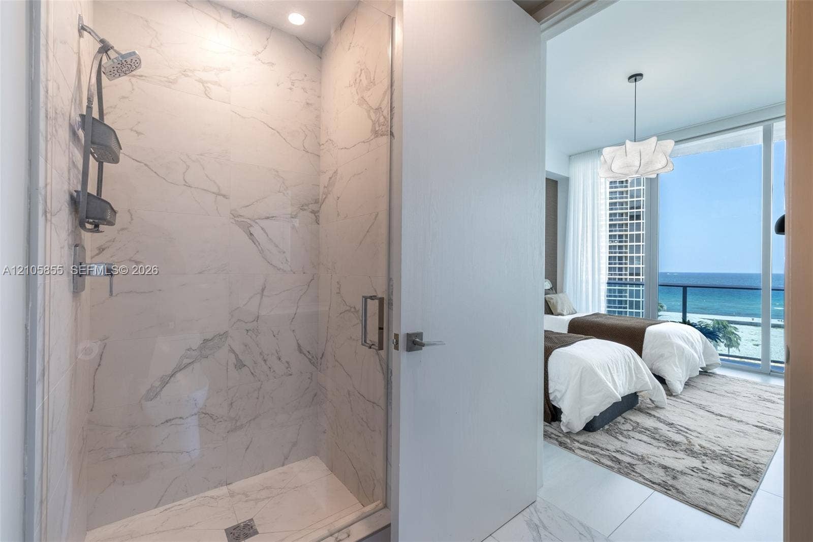 17550 Collins Avenue, #703, Sunny Isles Beach, Sunny Isles Beach, FL 33160 Walk-in shower featuring large-format stone-tile surround, glass enclosure, and ceiling-mounted light, accompanied by floor-to-ceiling windows and coastal water scenery