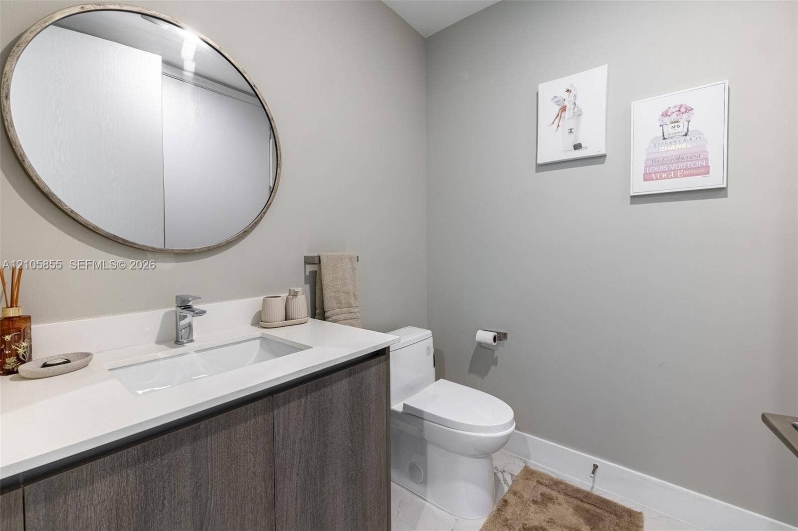 17550 Collins Avenue, #703, Sunny Isles Beach, Sunny Isles Beach, FL 33160 Floating vanity featuring a wood-finish cabinet and solid-surface countertop, integrated rectangular sink, chrome-finish faucet, and oval wall-mounted mirror