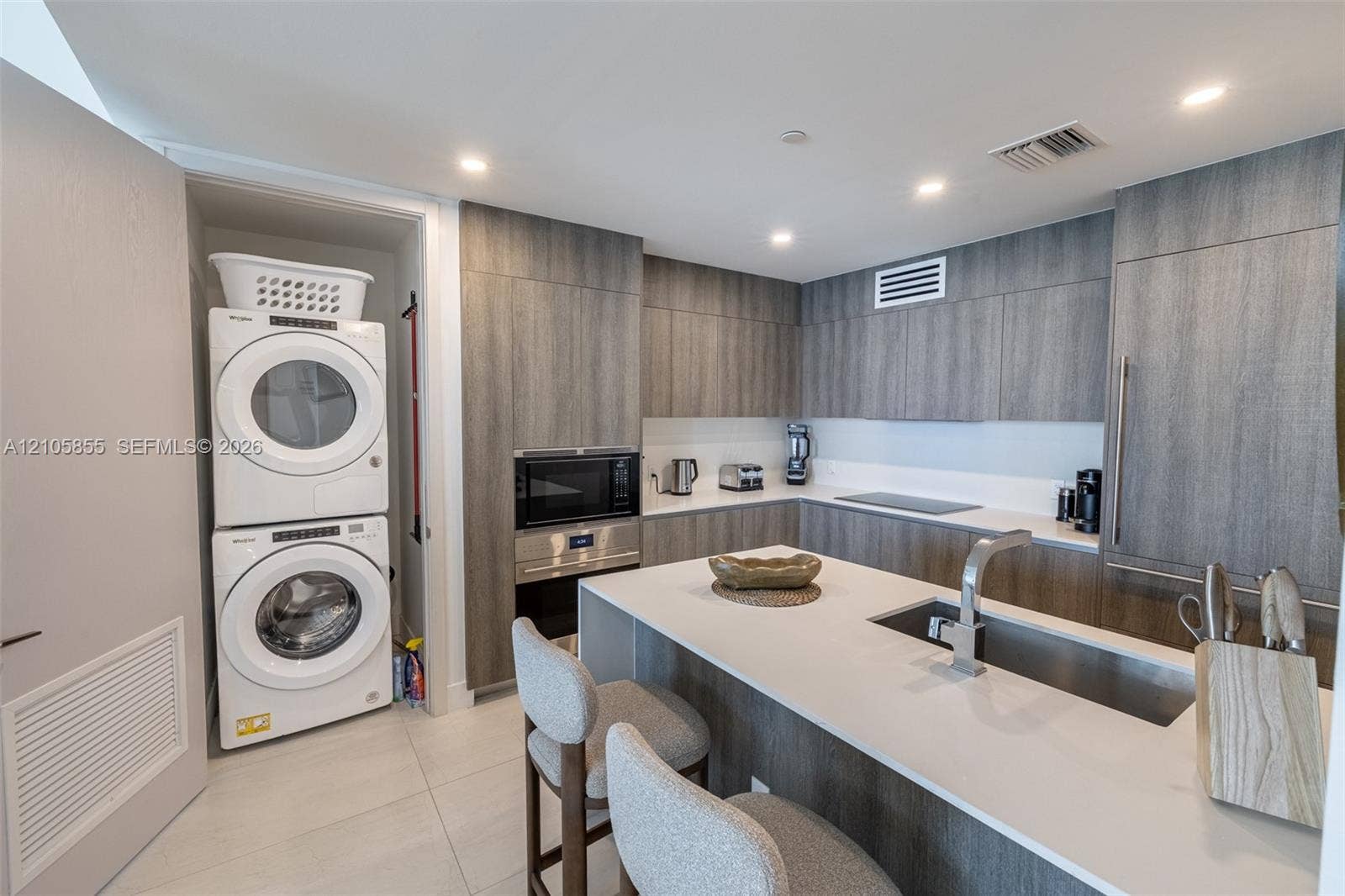 17550 Collins Avenue, #703, Sunny Isles Beach, Sunny Isles Beach, FL 33160 Kitchen featuring flat-panel wood-finish cabinetry, quartz countertops, an integrated island, built-in stainless steel appliances, and a stacked laundry unit