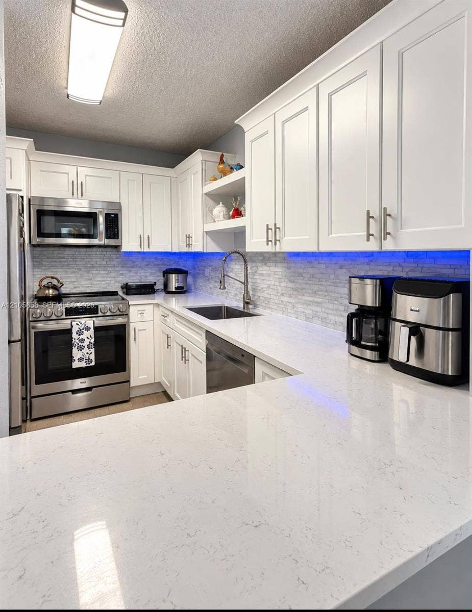 9471 Evergreen Place, #307, Davie, FL 33324 Kitchen featuring white shaker-style cabinetry, solid-surface countertops, a stainless steel appliance package, and a tiled backsplash with integrated under-cabinet lighting