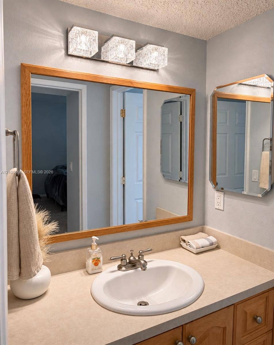 9471 Evergreen Place, #307, Davie, FL 33324 Bathroom vanity featuring a solid-surface countertop, an integrated drop-in sink, wood-finish cabinetry, a framed vanity mirror, and three-light geometric wall-mounted fixture