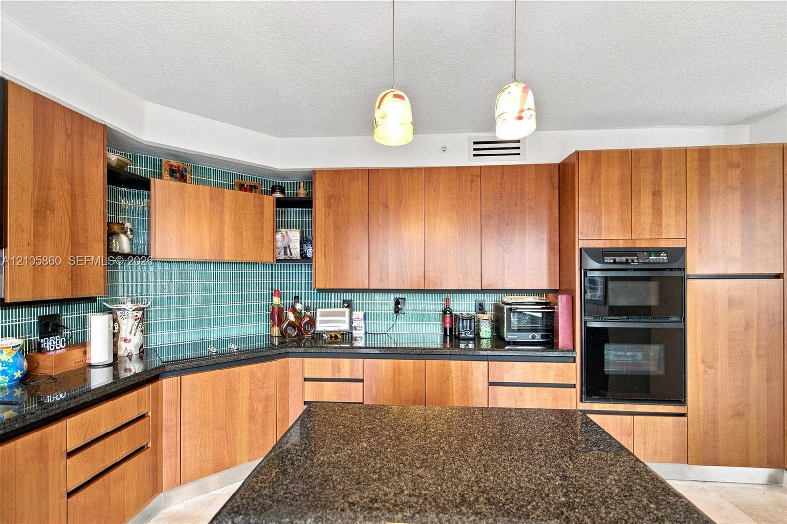 17555 Collins Avenue, #1903, Sunny Isles Beach, FL 33160 Kitchen featuring flat-panel wood cabinetry, dark stone countertops, a green glass tile backsplash, double wall ovens, and dual pendant lighting