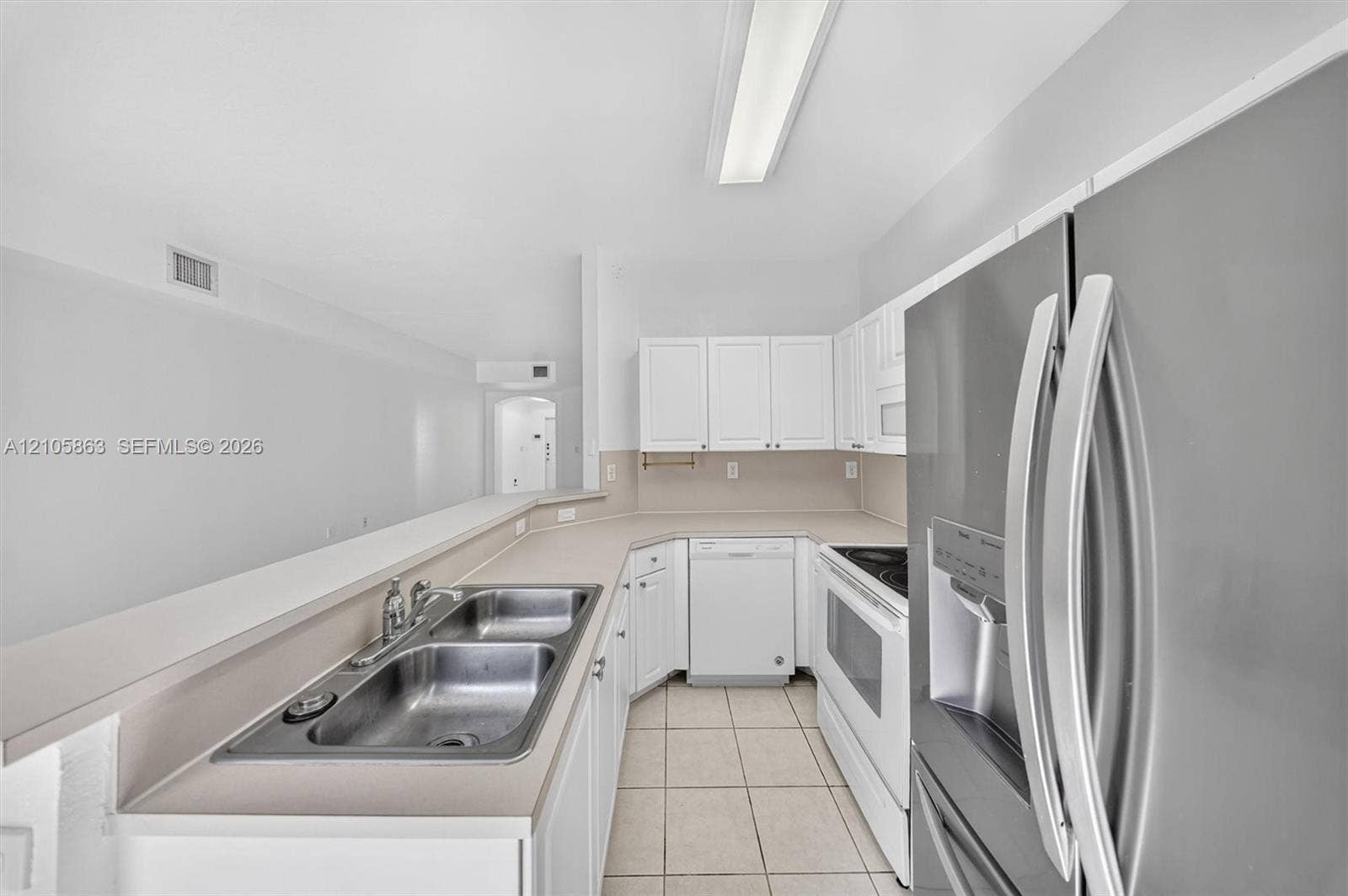 8846 W Flagler Street, #5, Miami, FL 33174 Kitchen featuring white cabinetry, solid-surface countertops, dual-basin stainless steel sink, tile flooring, and stainless steel refrigerator