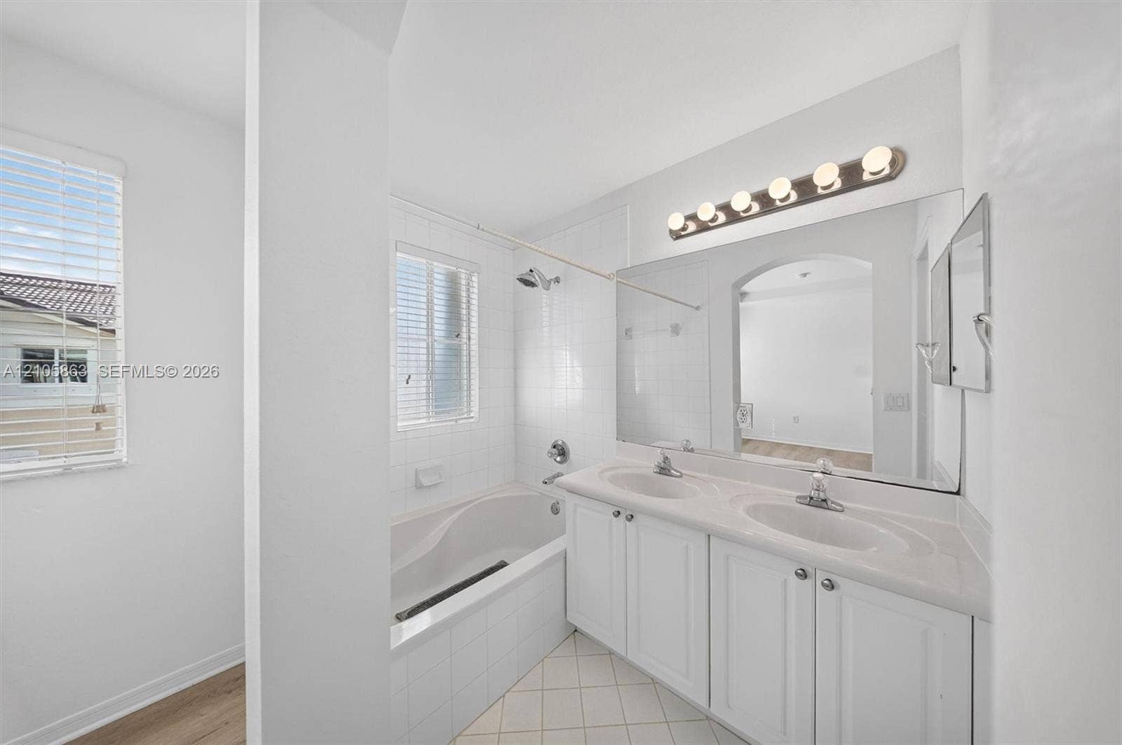 8846 W Flagler Street, #5, Miami, FL 33174 Dual-sink vanity with white cabinetry and a solid-surface countertop, full-width wall mirror, bathtub with white tile surround, and tile flooring