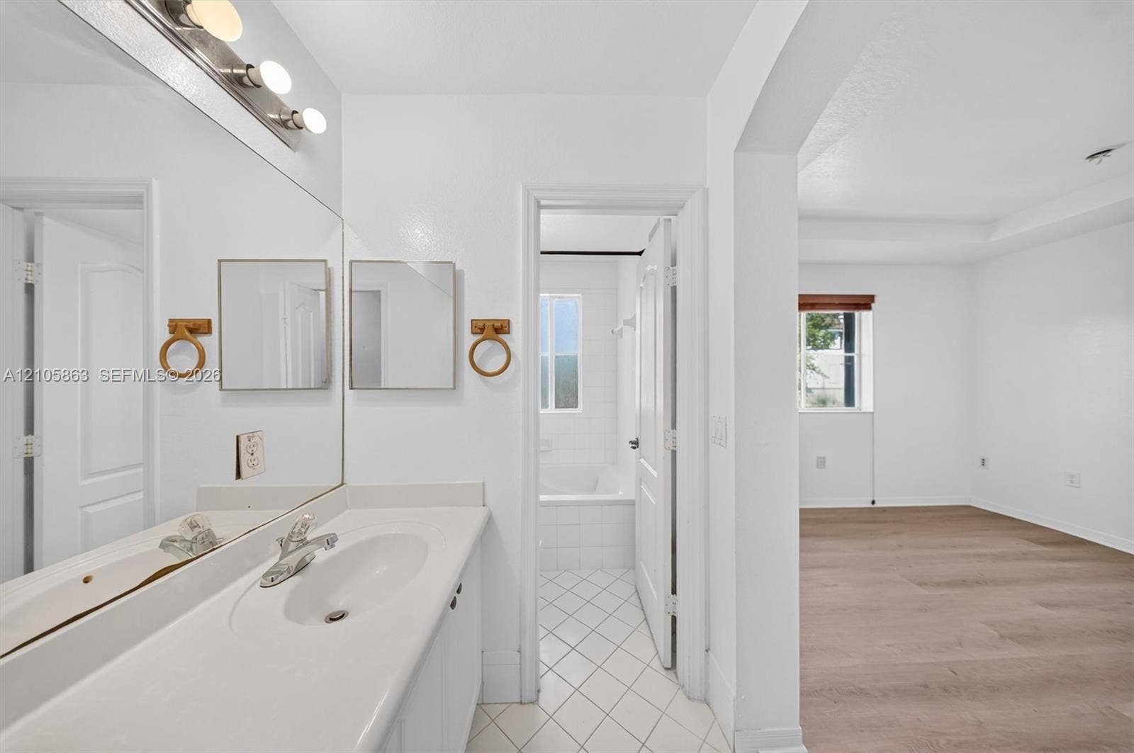 8846 W Flagler Street, #5, Miami, FL 33174 Full-width vanity with integrated sink, expansive wall-to-wall mirror, brushed metal fixtures, white tiled flooring, and wood-finish flooring