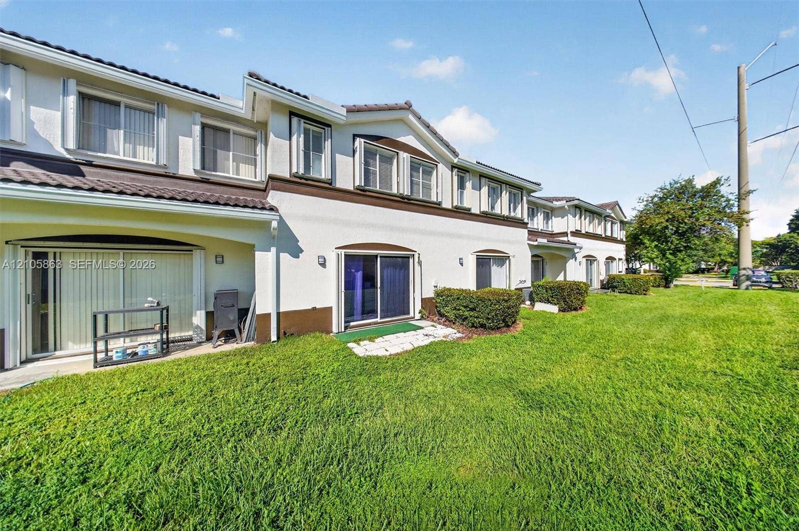 8846 W Flagler Street, #5, Miami, FL 33174 Multi-unit exterior featuring a stucco facade, dark-toned roof shingles, sliding glass doors, and established landscaping