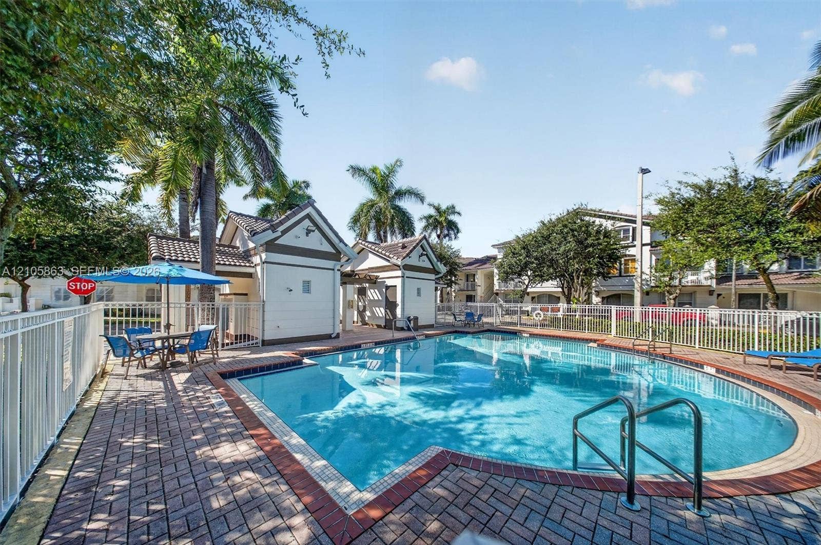 8846 W Flagler Street, #5, Miami, FL 33174 In-ground swimming pool with brick paver decking, white perimeter fencing, and two pool-side structures featuring pitched rooflines