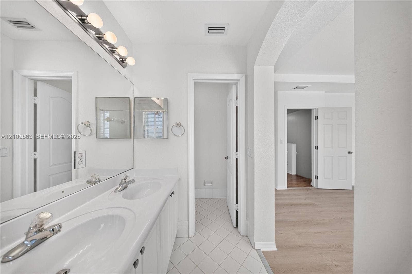 8846 W Flagler Street, #5, Miami, FL 33174 Dual-sink vanity with white countertop, full-width vanity mirror, polished chrome fixtures, white tile flooring, and arched architectural detailing
