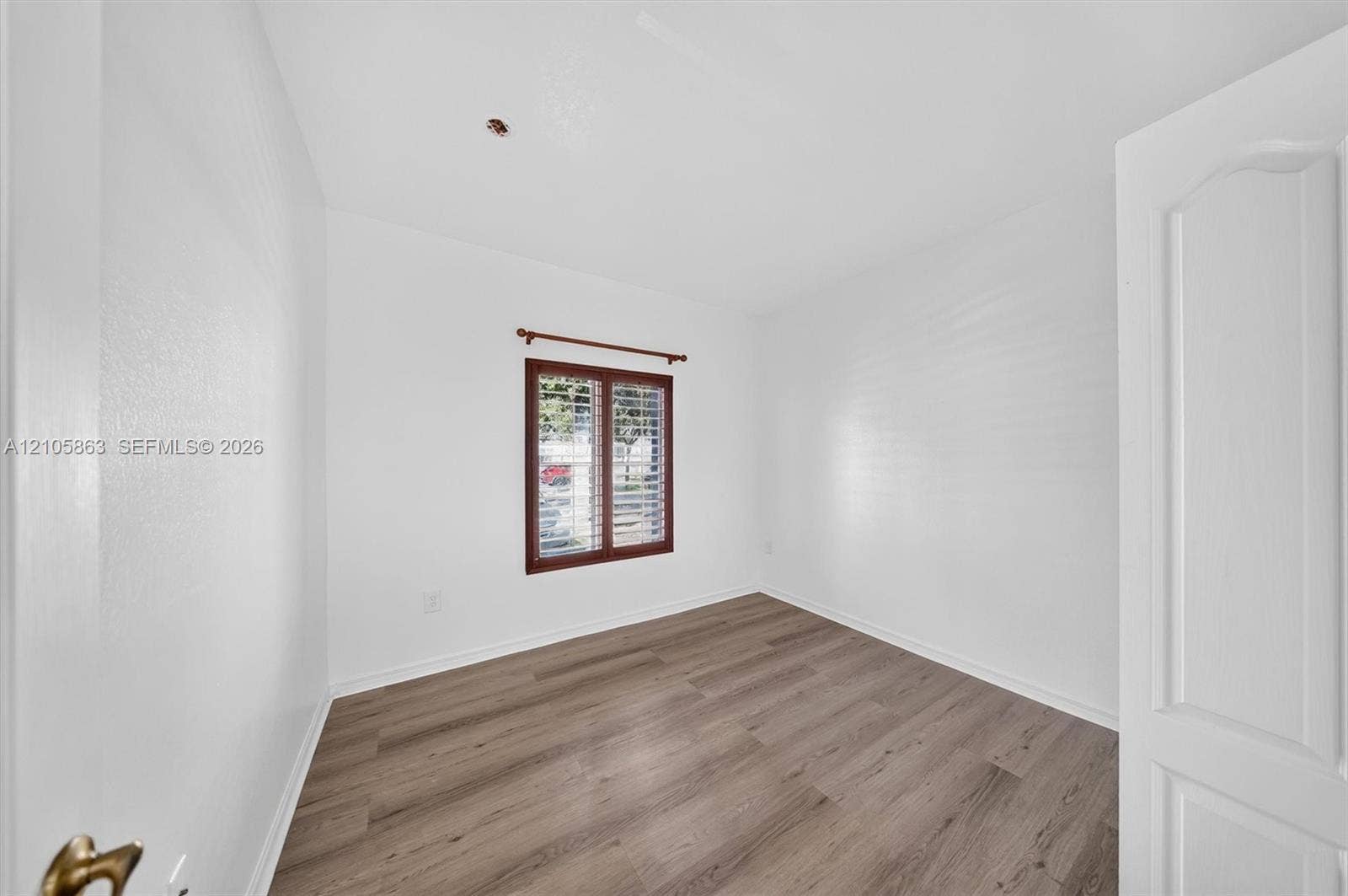 8846 W Flagler Street, #5, Miami, FL 33174 Room interior featuring wood-finish flooring, white walls, and a window equipped with plantation shutters and a wooden curtain rod