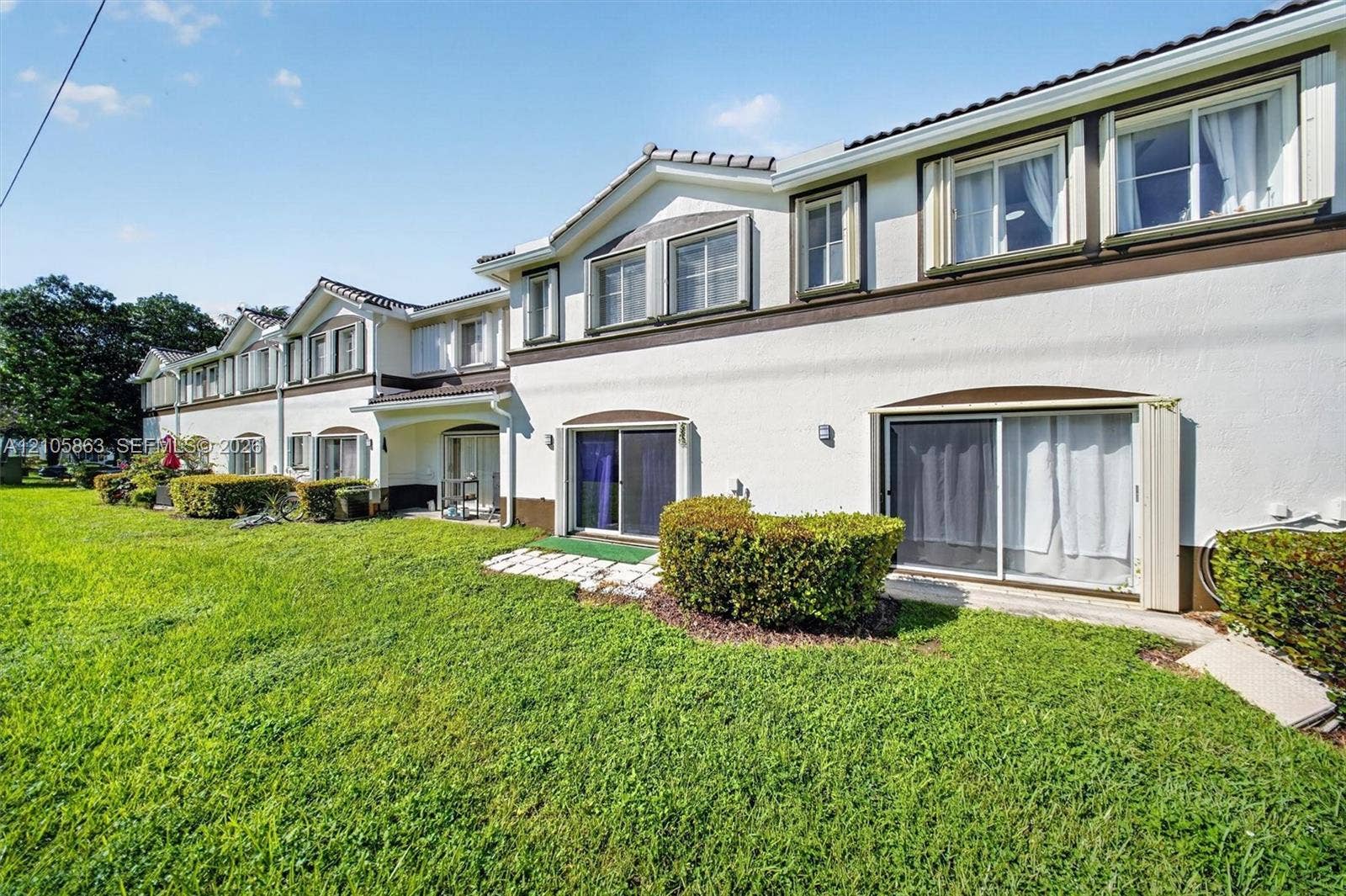 8846 W Flagler Street, #5, Miami, FL 33174 Stucco exterior featuring multi-gabled rooflines, stone-tiled patio accents, sliding glass door entryways, and expansive shared lawn space