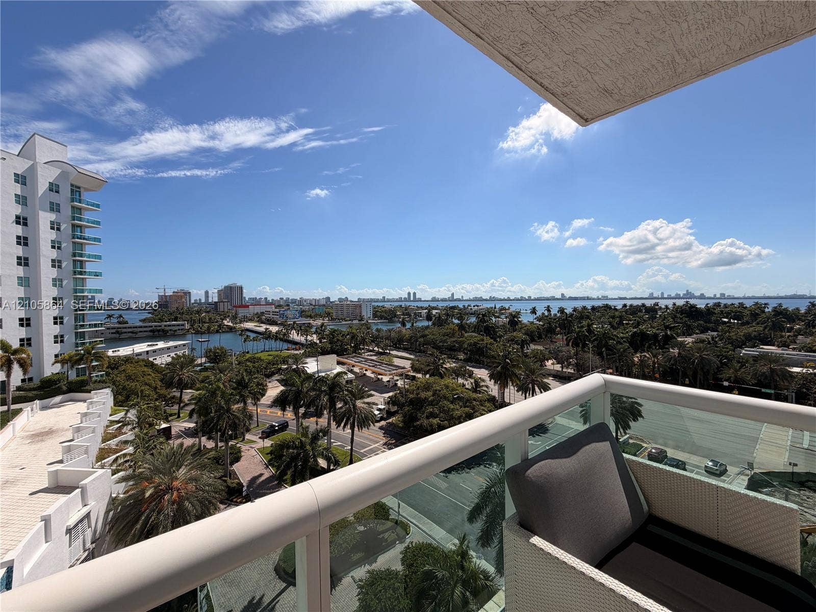 Private balcony featuring a glass and white metal railing, overlooking urban and coastal scenery
