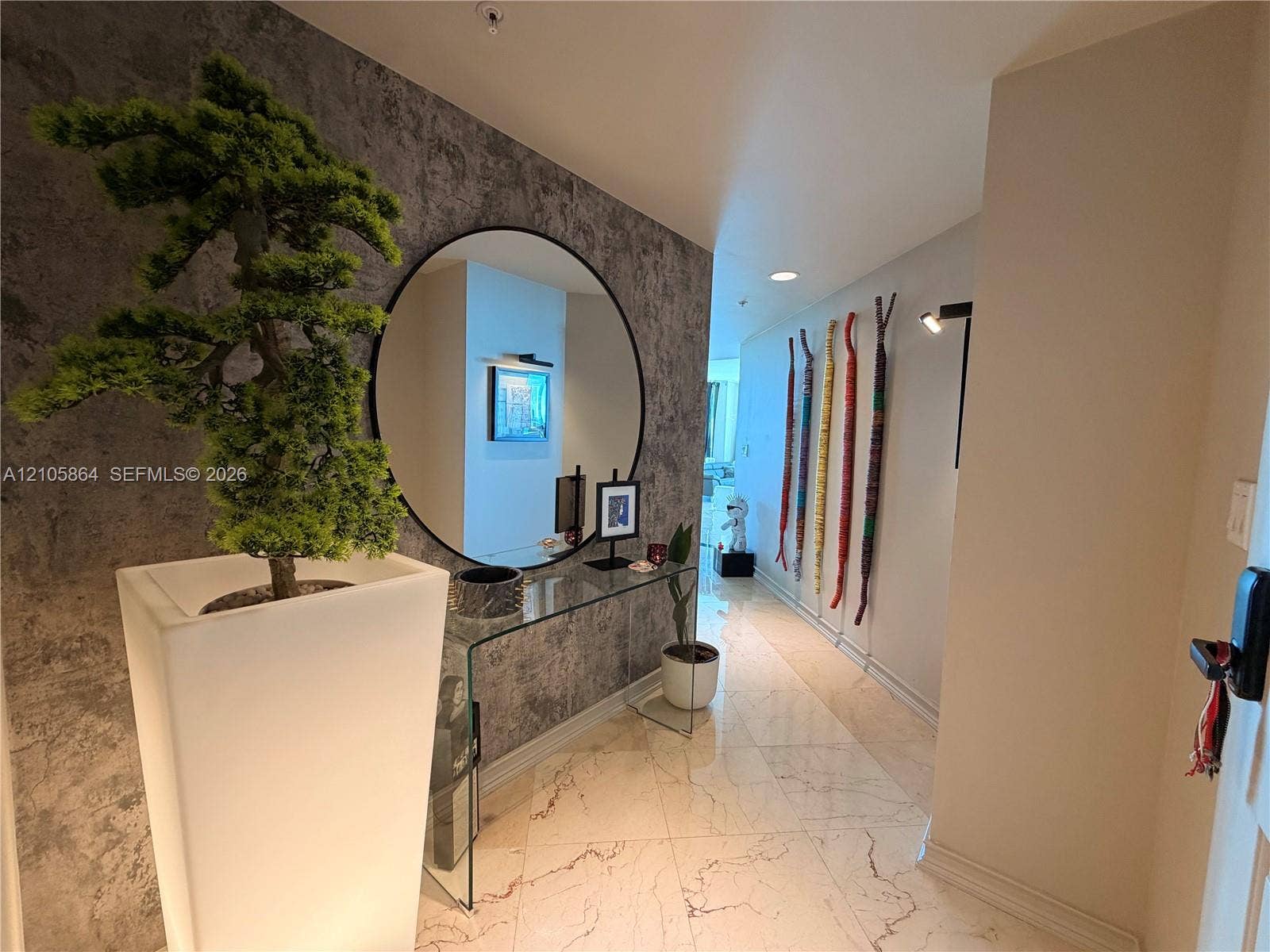 Entryway featuring polished stone flooring, a textured accent wall, a circular wall-mounted mirror, and recessed lighting