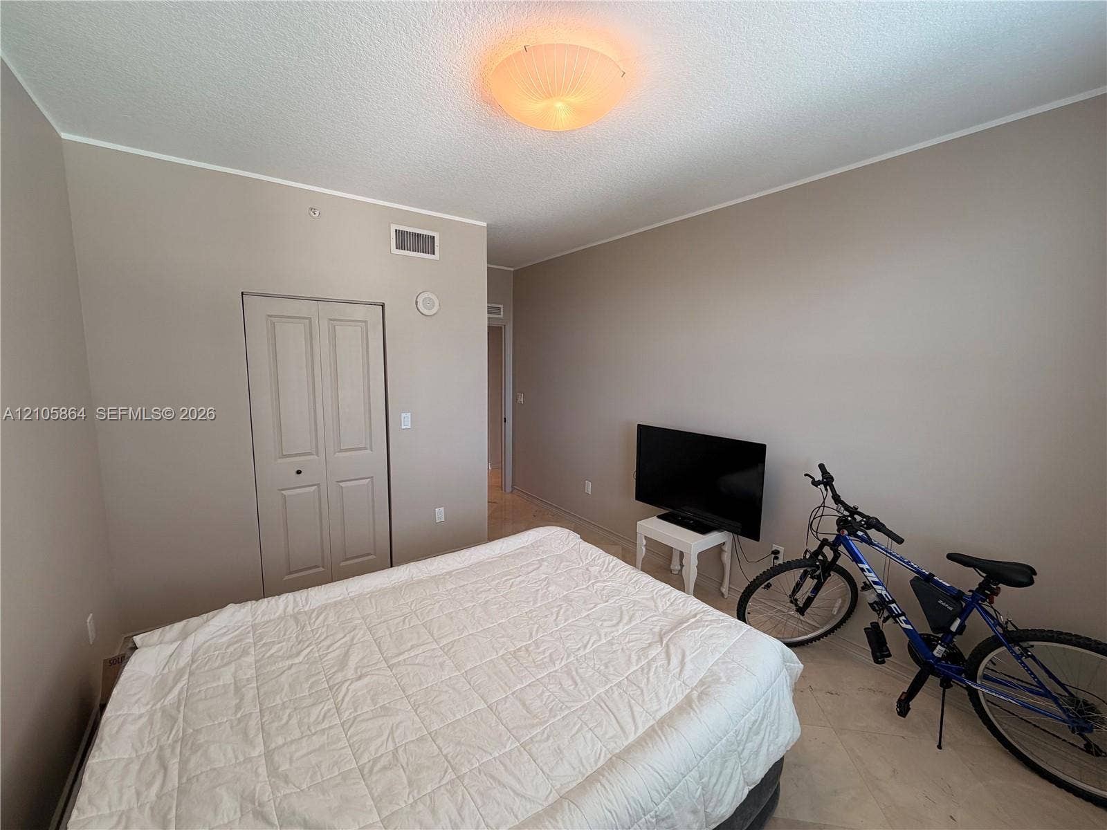 Neutral-toned interior space featuring light-colored tile flooring, bi-fold closet doors, and a flush-mount dome light fixture