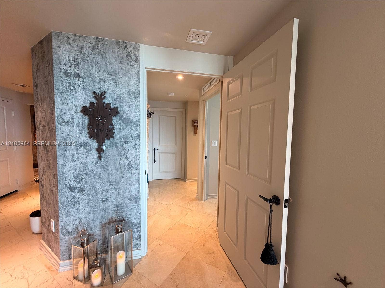Textured accent wall with a grey stone-finish veneer, complemented by neutral tile flooring laid on a diagonal pattern and six-panel interior doors with matte black hardware