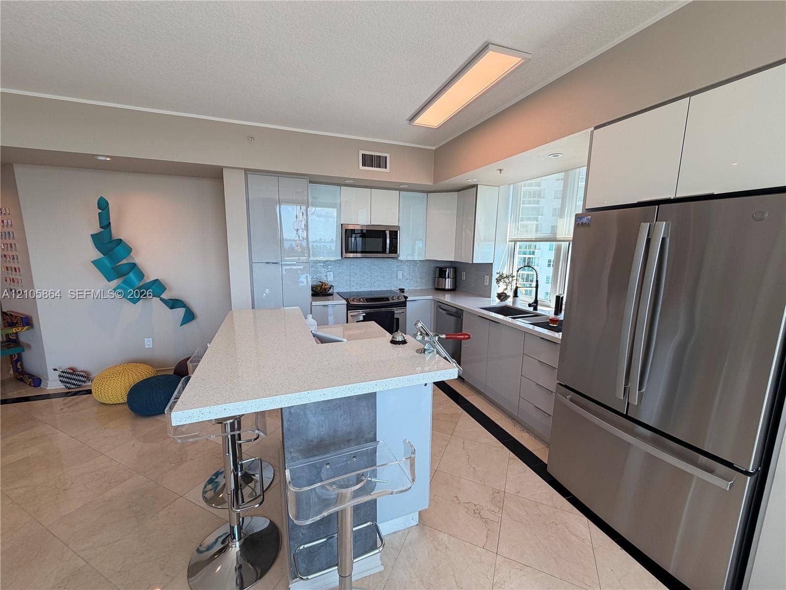 Kitchen featuring a stone-surface island, high-gloss cabinetry, stainless steel appliances, and tiled flooring
