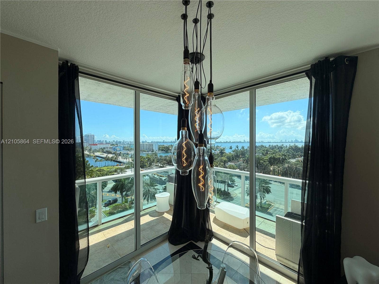 Floor-to-ceiling corner windows with sliding glass doors, multi-pendant Edison-style light fixture, and wraparound balcony with metal railing
