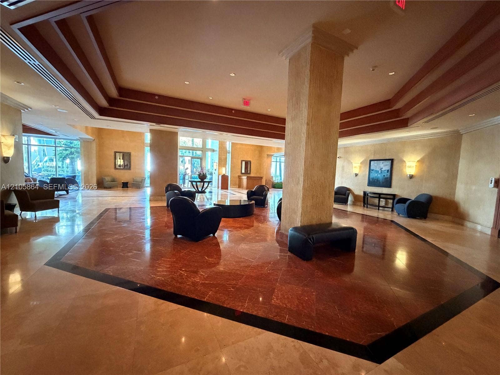 Grand lobby featuring multi-tiered tray ceilings, polished stone flooring with geometric inlays, a central structural column, and recessed perimeter lighting