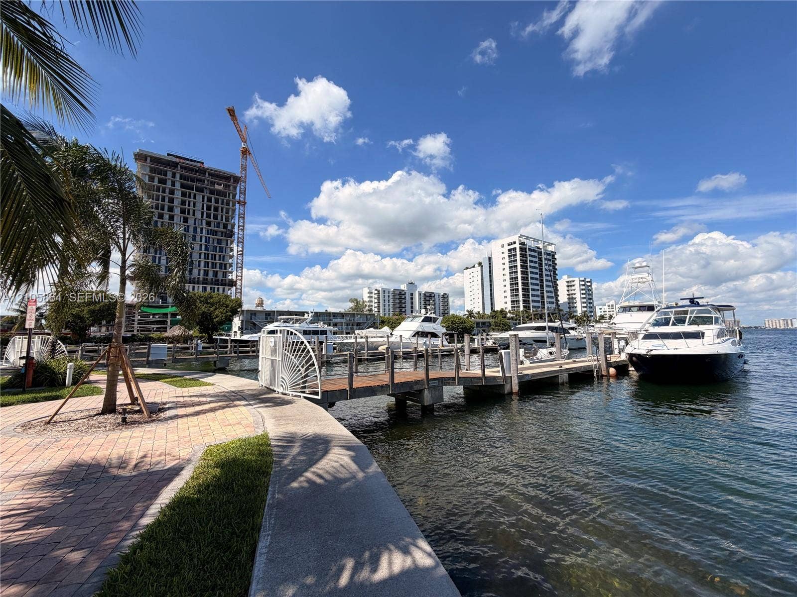 Waterfront property featuring a private wooden dock, concrete seawall, brick-paver walkway, and mature palms