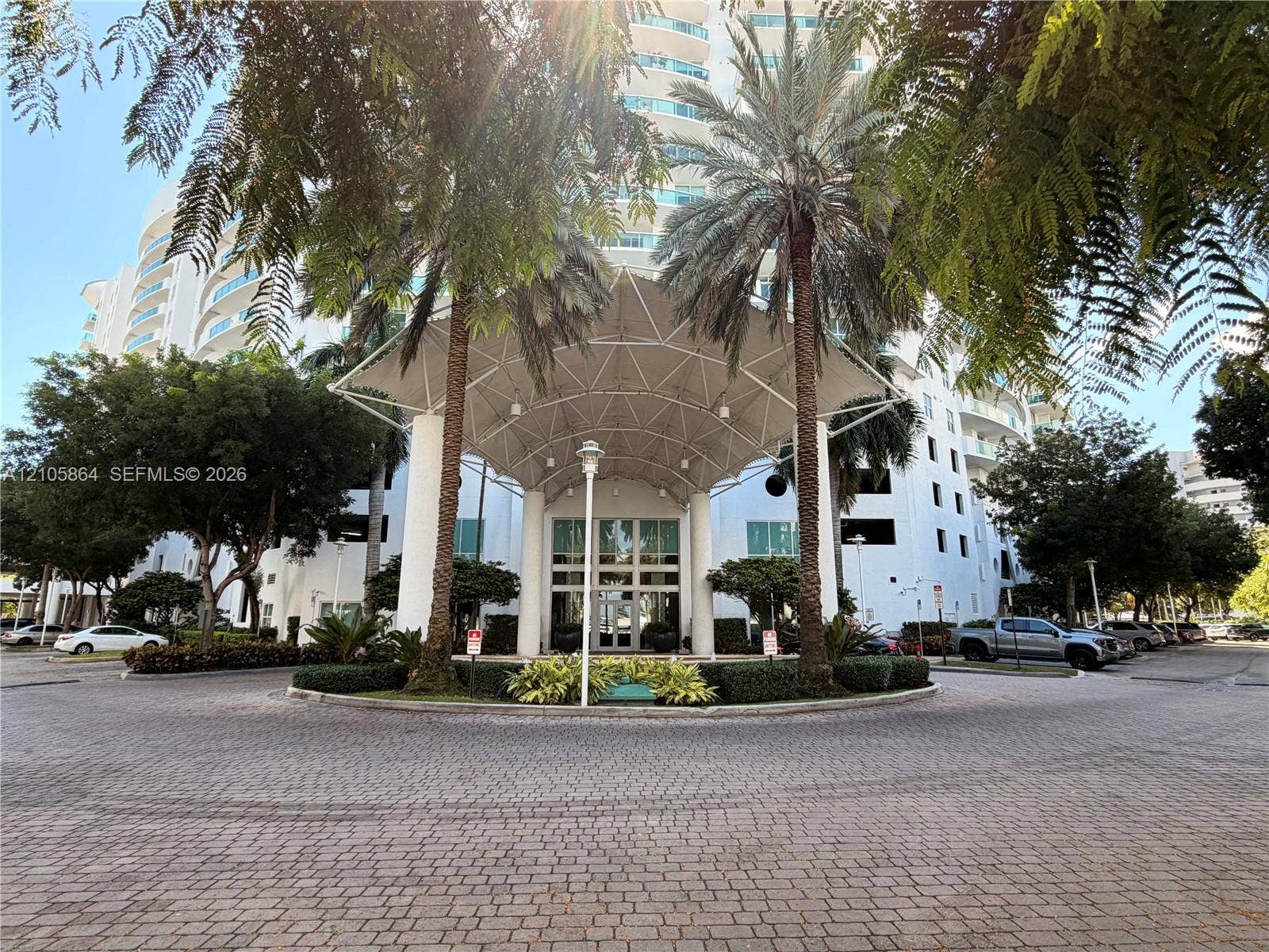 High-rise building exterior featuring a covered porte-cochre entrance, glass-paneled double doors, paved circular drive, and landscaped grounds