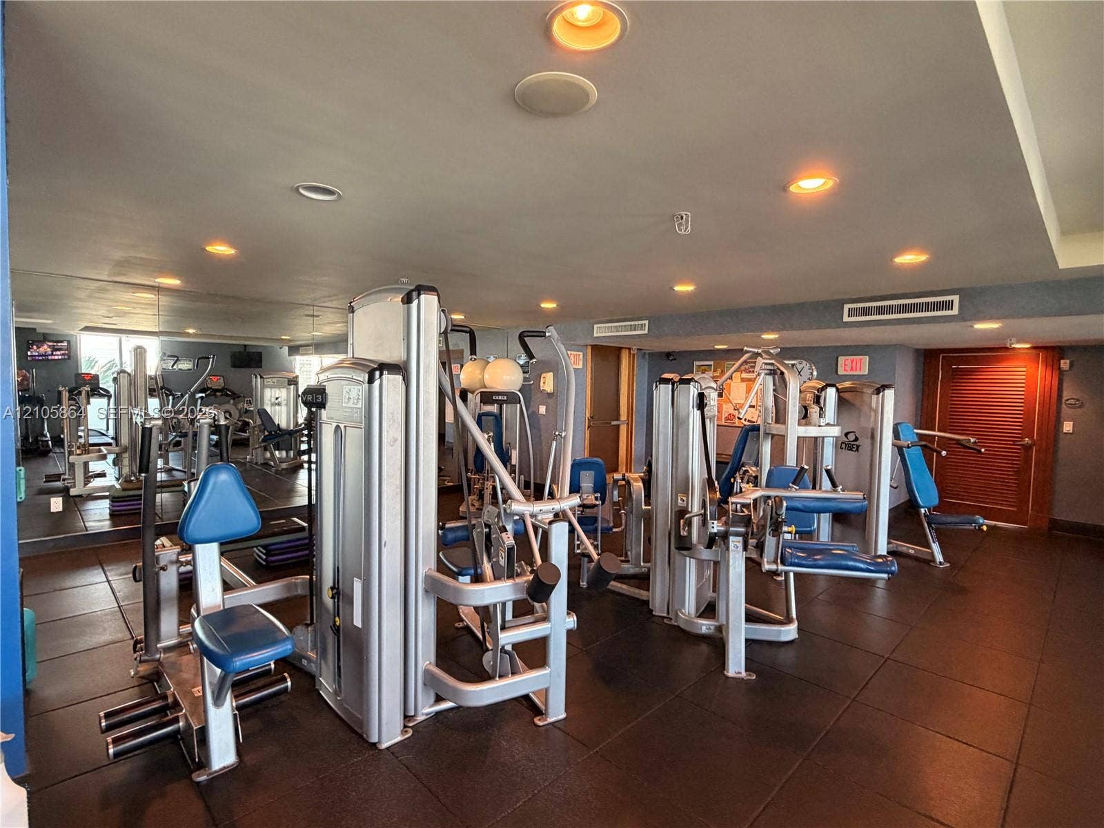 Fitness room featuring rubberized flooring, recessed lighting, mirrored walls, and solid-wood door
